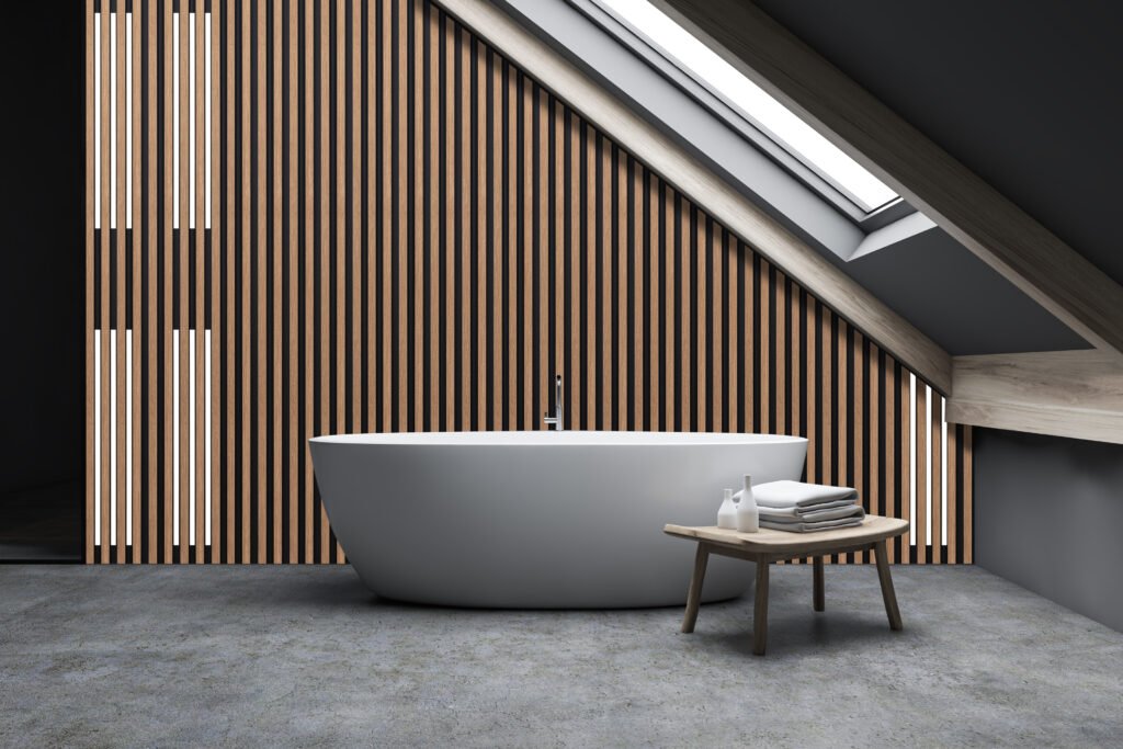 Interior of minimalistic attic bathroom with grey walls, concrete floor and comfortable bathtub standing under window in the roof with bench beside it. 3d rendering